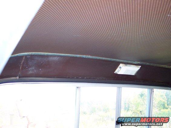 Interior view of a vehicle's headliner and upper dashboard area, showing a patterned headliner and a small light fixture