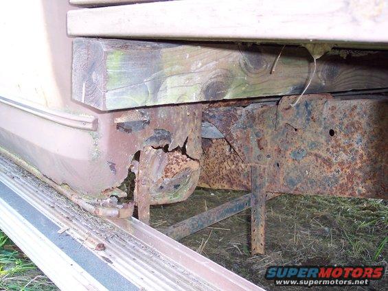 Rusted frame and wooden support under a vehicle, showing significant corrosion