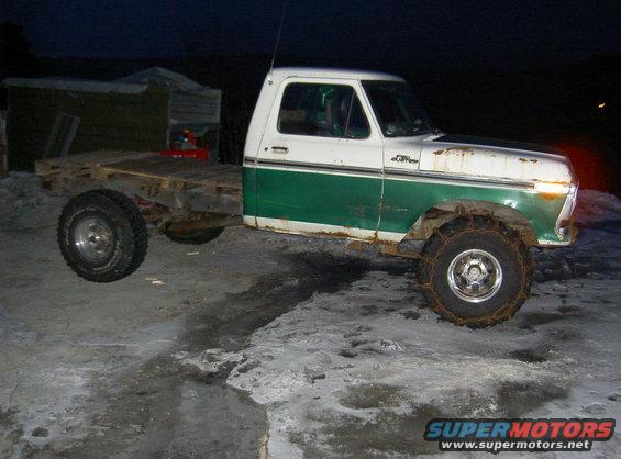 White and green Ford pickup truck with a flatbed, snow chains on front tires