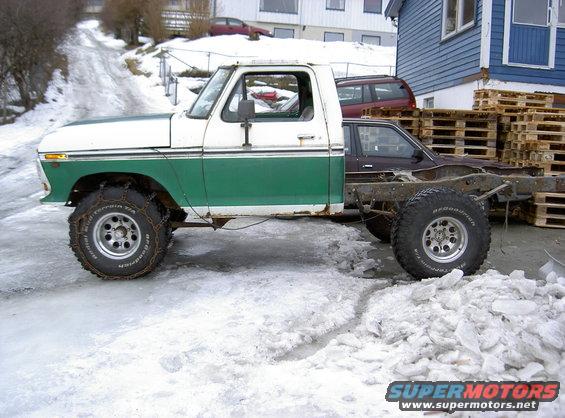 White and green 1979 Ford F-150 truck cab with a bare chassis and rear wheels, parked on icy ground