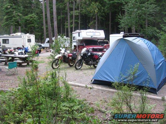 Two dirt bikes parked at a campsite with RVs and a tent