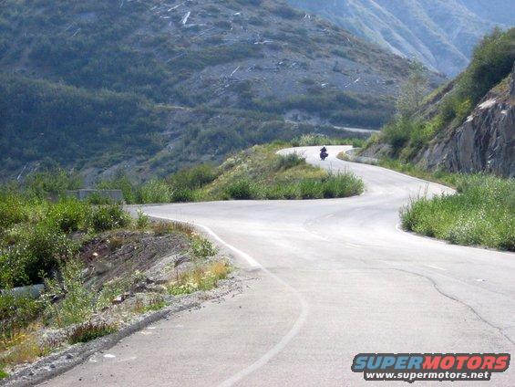 Motorcycle navigating a sharp curve on a paved mountain road with sparse vegetation