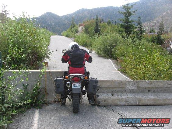 Motorcycle with saddlebags stopped at a concrete barrier on a paved road