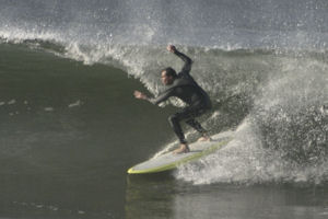 Surfer in a black wetsuit on a yellow surfboard carves a wave