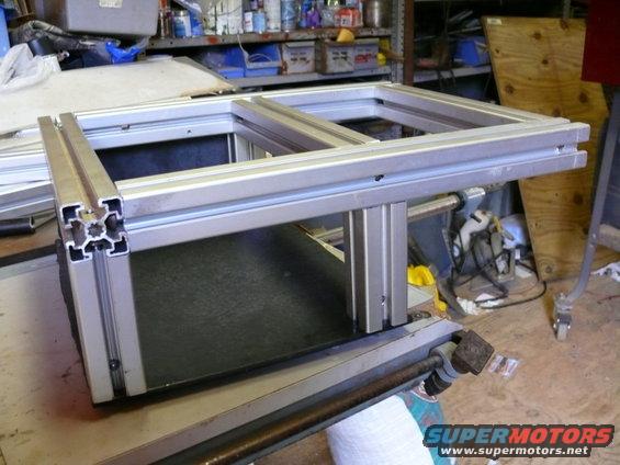 Aluminum extrusion frame assembly on a workbench, with shelves and tools in the background