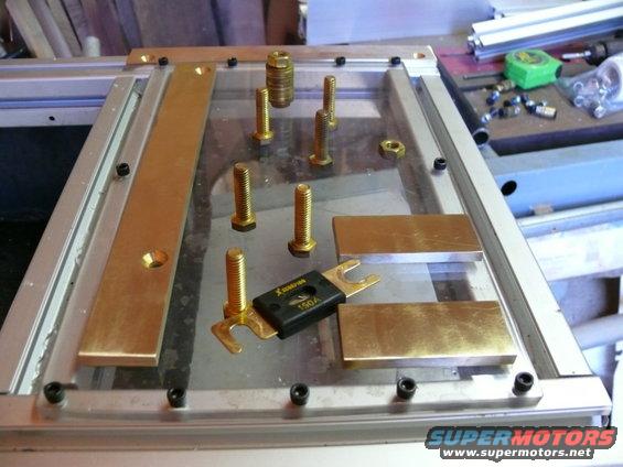 Battery fuse and brass mounting hardware on a clear plate with metal frame