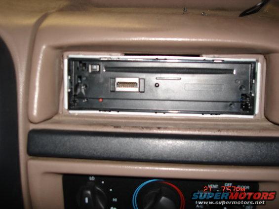 Car stereo opening with mounting bracket and some wiring visible. Controls for climate are below