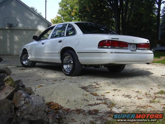 White 1997 Ford Crown Victoria sedan with chrome wheels parked on a dirt driveway