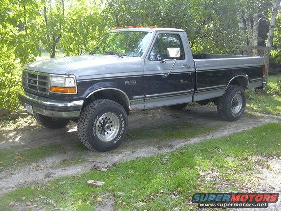 Two-tone grey and dark blue Ford F-250 pickup truck with chrome wheels and off-road tires, parked on a dirt and grass driveway
