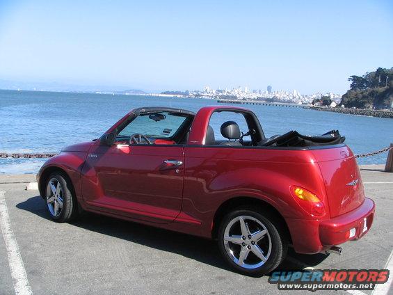 Red 2005 Chrysler PT Cruiser convertible parked by the water with a city skyline in the background