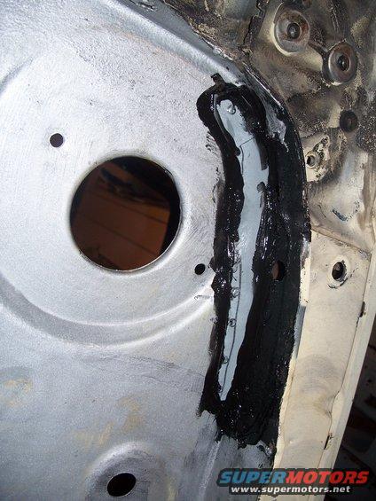 Close-up of a vehicle's metal chassis with black sealant applied over a repair