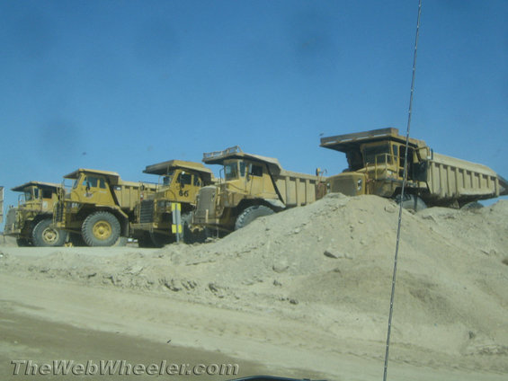 line of yellow mining dump trucks parked on dirt with blue sky