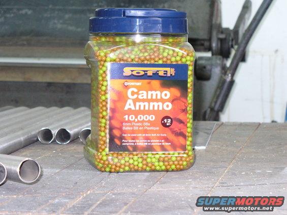 Jar of 10,000 6mm plastic BBs labeled Camo Ammo, on a wooden surface with metal pipes
