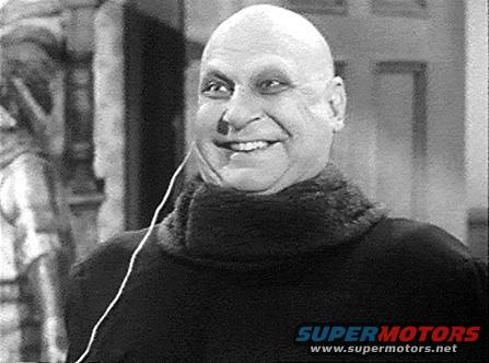 bald man with a wide smile and a dark turtleneck, wearing an earphone