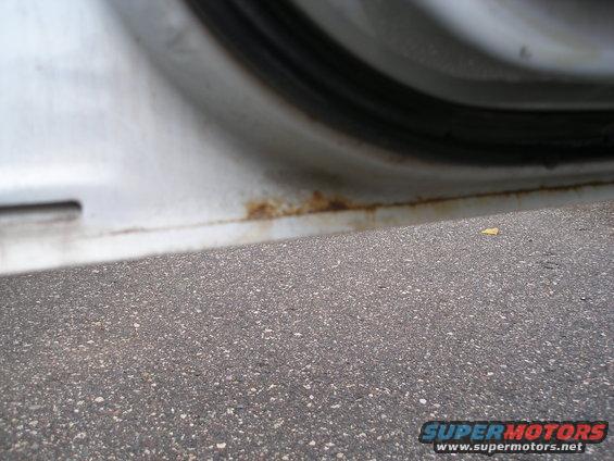 White car door sill with rust spots and asphalt in foreground