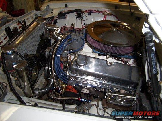 Engine bay view of a V8 engine with chrome valve covers, air filter, and radiator