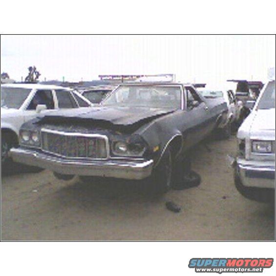 Dark coupe utility with damaged front end parked in a junkyard next to other vehicles