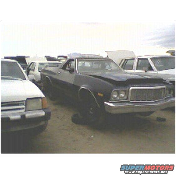 Dark blue 1972 Ford Ranchero with a dented hood and chrome grille, parked in a junkyard