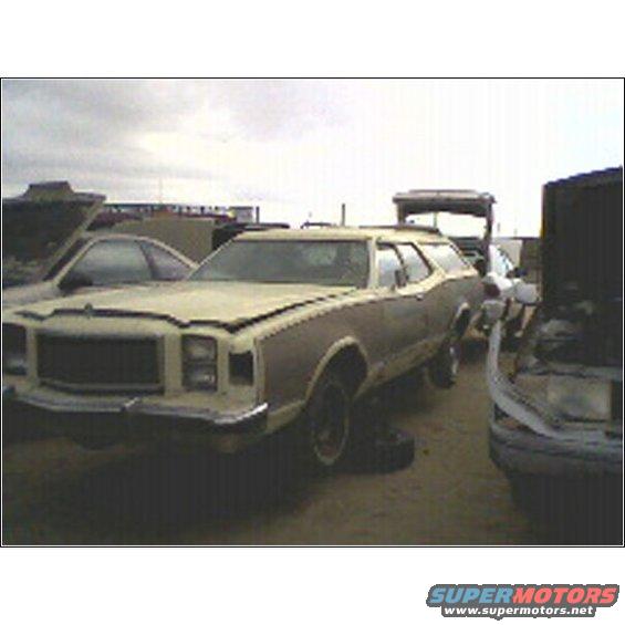 Station wagon with wood paneling, tan and brown, front 3/4 view, in a junkyard with other vehicles