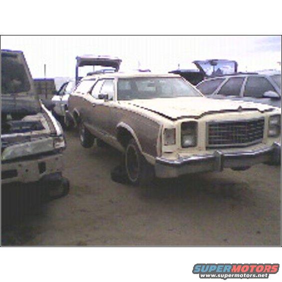 Beige station wagon with wood paneling, front end visible, in a junkyard