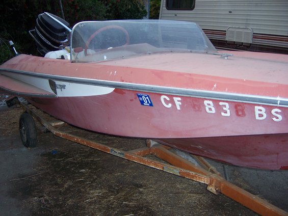 red boat on rusty trailer, outboard motor visible