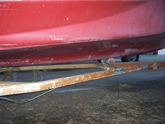 red boat on rusty trailer with visible wheels and rollers
