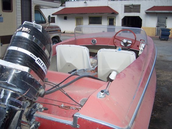 Red boat with a Mercury outboard motor and two white seats, parked next to an RV