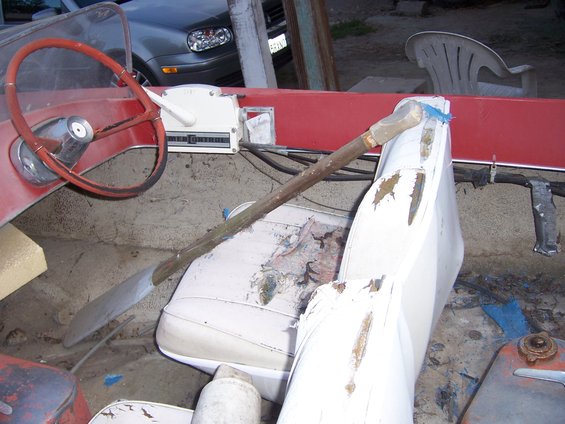 Boat interior with red trim, white seats, and a steering wheel. A wooden oar rests across the seats