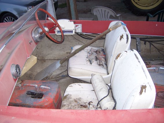 Interior of a red boat with white seats, steering wheel, and a paddle