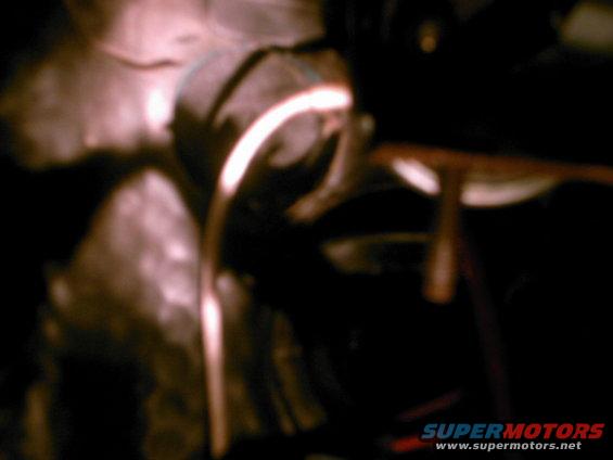 Close-up of a car's interior, possibly a dashboard or engine bay component, with a bright light source illuminating a curved metal or plastic piece
