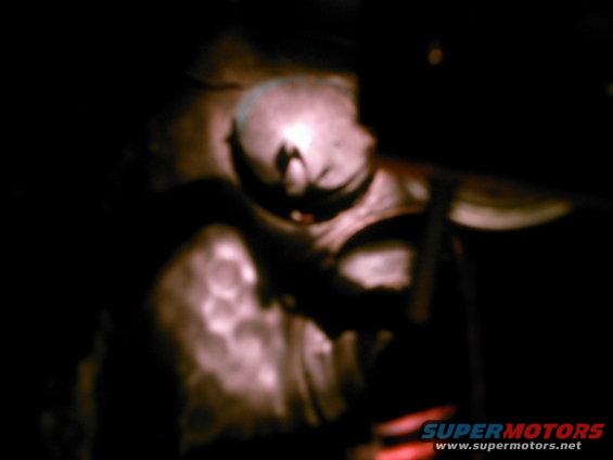 person's head and shoulders visible, working on car engine in dark garage