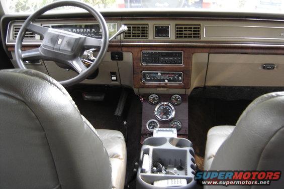 Car interior with tan leather seats, wood grain trim, and aftermarket gauges. The dashboard shows a radio and vents