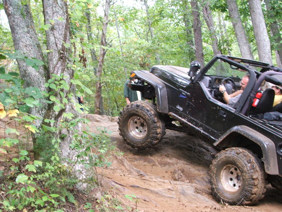 Black Jeep Wrangler climbing a rocky trail in a wooded area