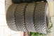 1986 Ford Bronco - Four off-road tires are stacked on their sides on a paved surface.