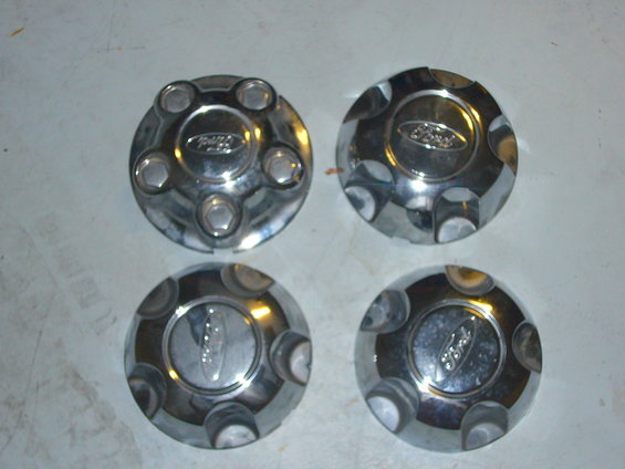 Four chrome Ford hubcaps with the Ford oval logo visible