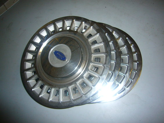Three silver Ford hubcaps with blue oval logo stacked on a gray surface