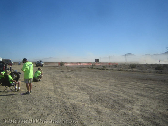 People in neon shirts at an off-road event with dust in the air and mountains in the background