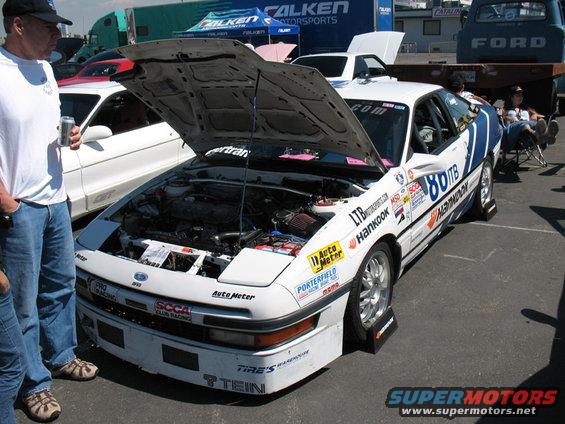 White race car with hood open, covered in sponsor decals