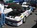 1995 Ford Probe - A white race car, likely a Ford Probe, is displayed with its hood open, its engine and numerous sponsor decals.