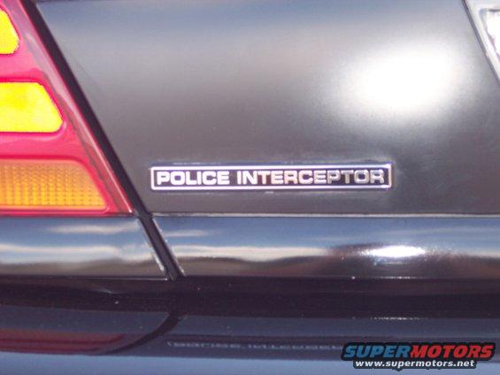 Close-up of a dark car's rear quarter panel showing a 'POLICE INTERCEPTOR' badge and part of a taillight