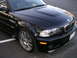 2002 BMW M3 - A black BMW M3 convertible is parked on asphalt, with reflections of trees in its paint.