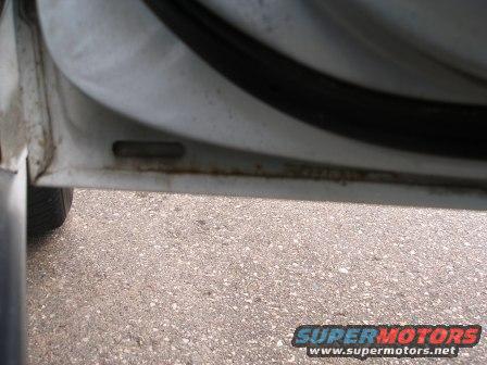 Close-up of a car's door jamb with visible rust and a black rubber seal
