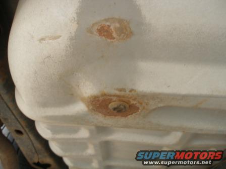 Underside of a white vehicle part with rust spots and a bolt