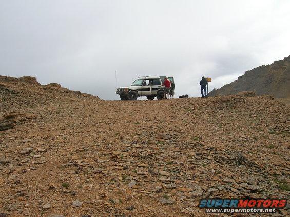 Two SUVs parked on a rocky hill with people standing around