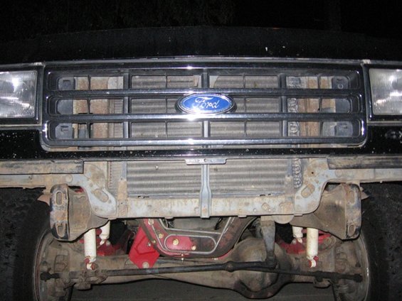 Front grille and suspension of a black Ford Bronco with a blue Ford emblem. The grille has horizontal bars and is slightly rusted