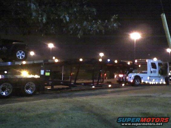 Dark SUV on car carrier truck at night