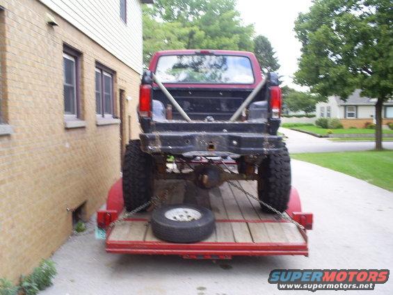 Red pickup truck with large tires on a red trailer, viewed from the rear