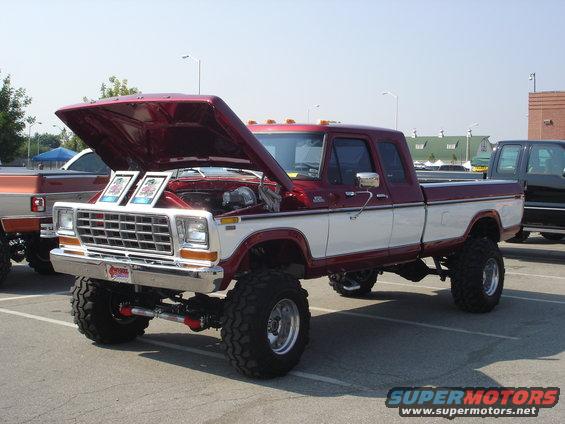 1979 Ford F-350 pickup truck, lifted, with hood open showing engine. Two framed photos are on display in the engine bay