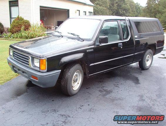 Black pickup truck with a camper shell, parked on a driveway in front of a house