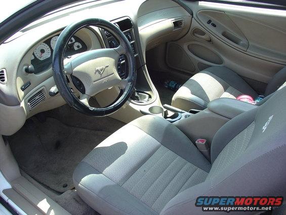 Car interior showing dashboard, steering wheel with Mustang logo, and fabric seats